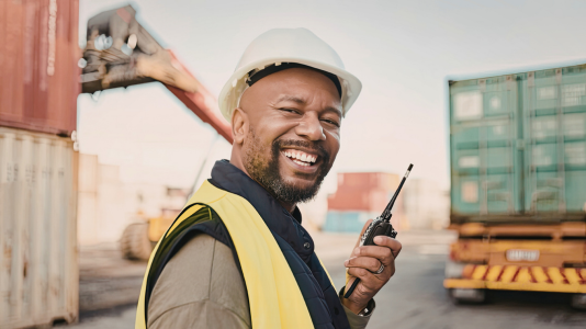 A construction worker in a hard hat and safety vest smiling on a job site, representing ProServeIT's IT services for the construction industry