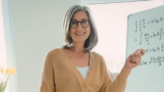 A teacher smiling while writing on a whiteboard, representing ProServeIT's IT services for the education sector