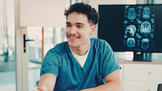 A healthcare professional in scrubs smiling in a clinical setting, representing ProServeIT's IT services for the healthcare industry