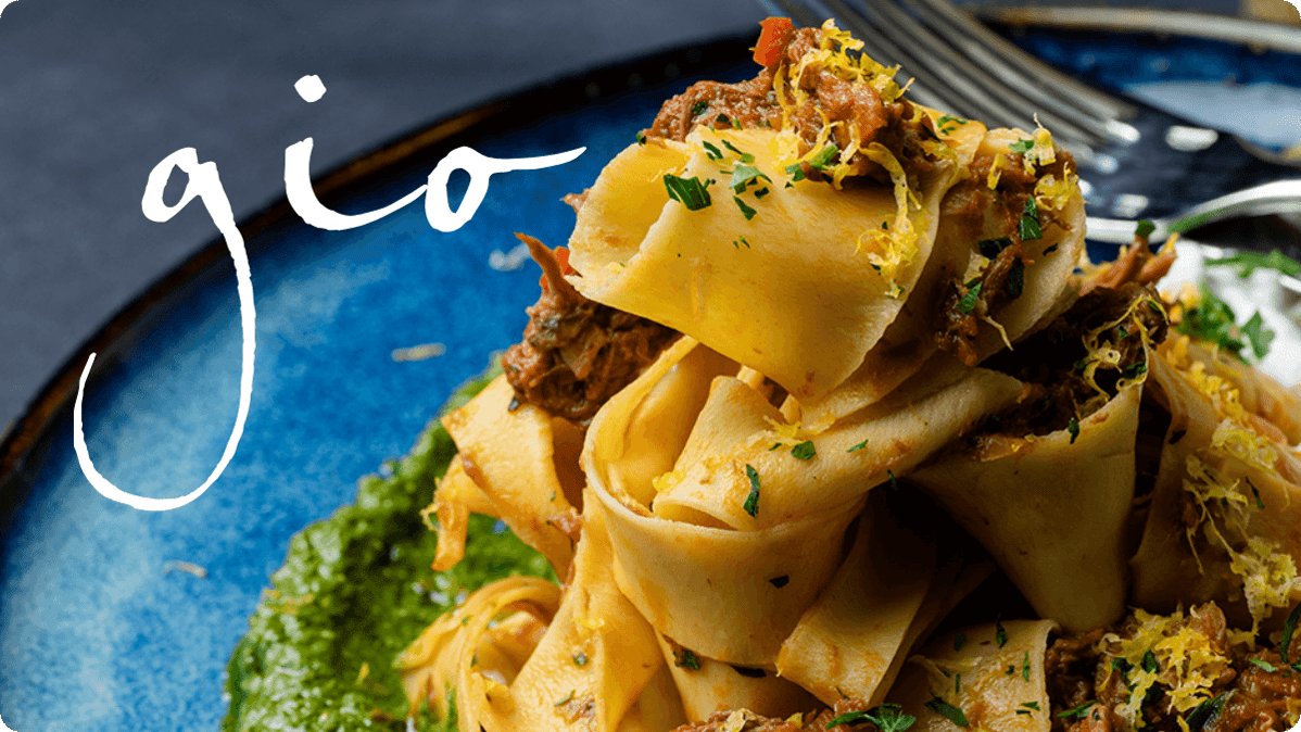 Close-up of handmade pappardelle pasta topped with slow-braised meat, fresh herbs, and citrus zest, served on a vibrant blue plate at Gio restaurant in Halifax
