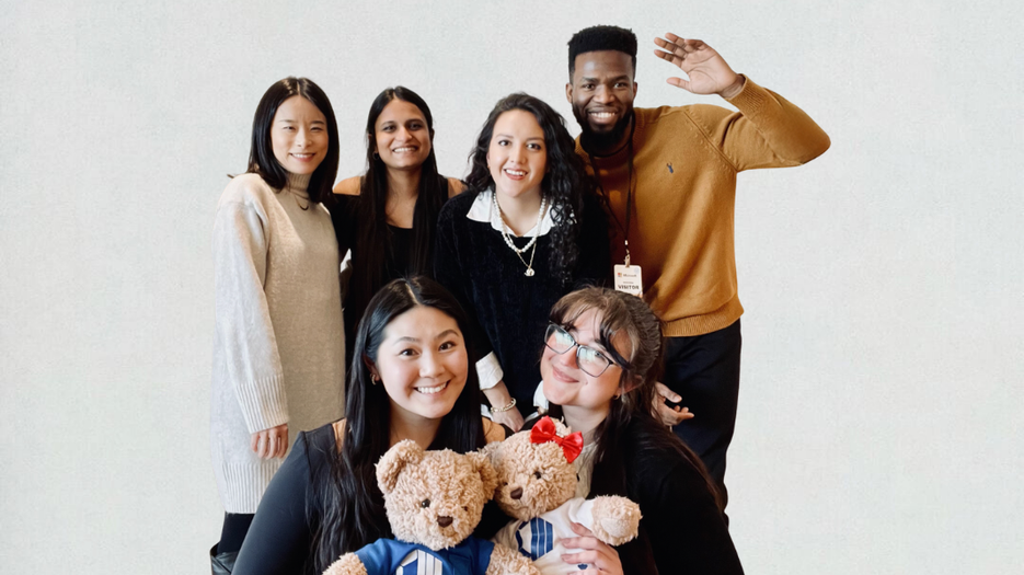 Marketing Team at Event - team group photo with six colleagues posing together indoors, holding branded teddy bears