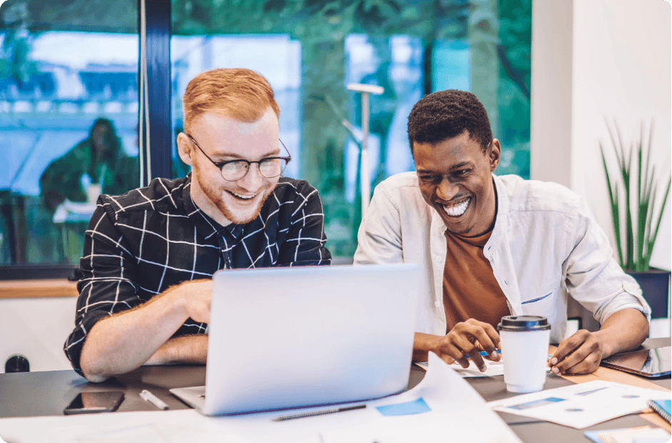Two colleagues laughing together while reviewing work on a laptop, representing the competitive edge ProServeIT's strategic technology services deliver to growing organizations
