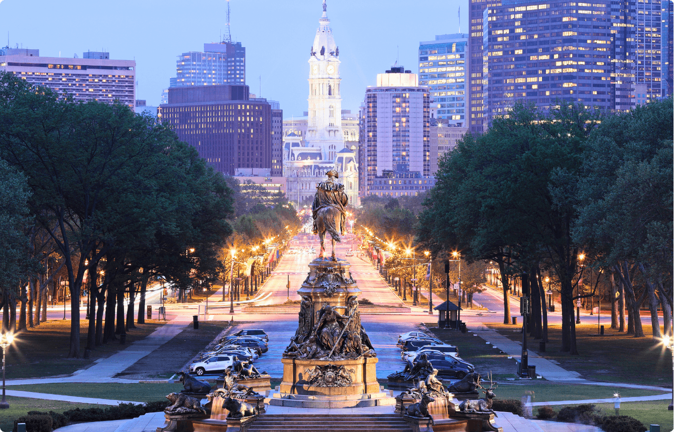 Philadelphia skyline along Benjamin Franklin Parkway at dusk, with illuminated fountains, tree-lined streets, and downtown buildings, representing the location of the AI Copilot EBS event.