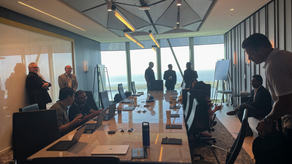 Professionals meeting in a boardroom during a ProServeIT AI EBS event for CFOs, with laptops, presentation materials, and a city skyline visible through large windows.